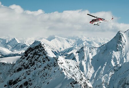 Helicopter soaring above majestic snow-covered mountain peaks under a clear blue sky