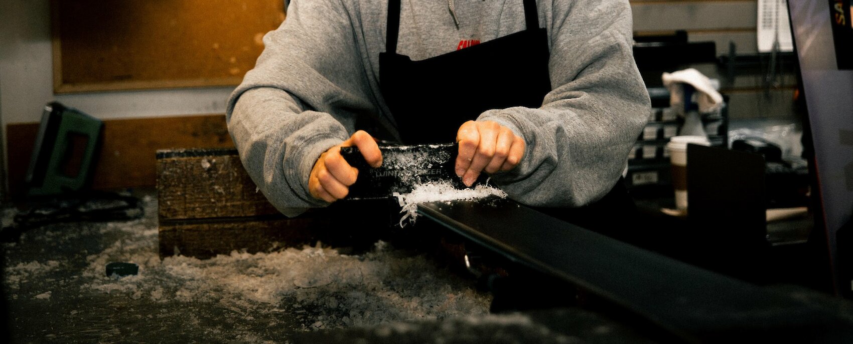 Person sharpening skis with a file in a workshop, surrounded by ski equipment