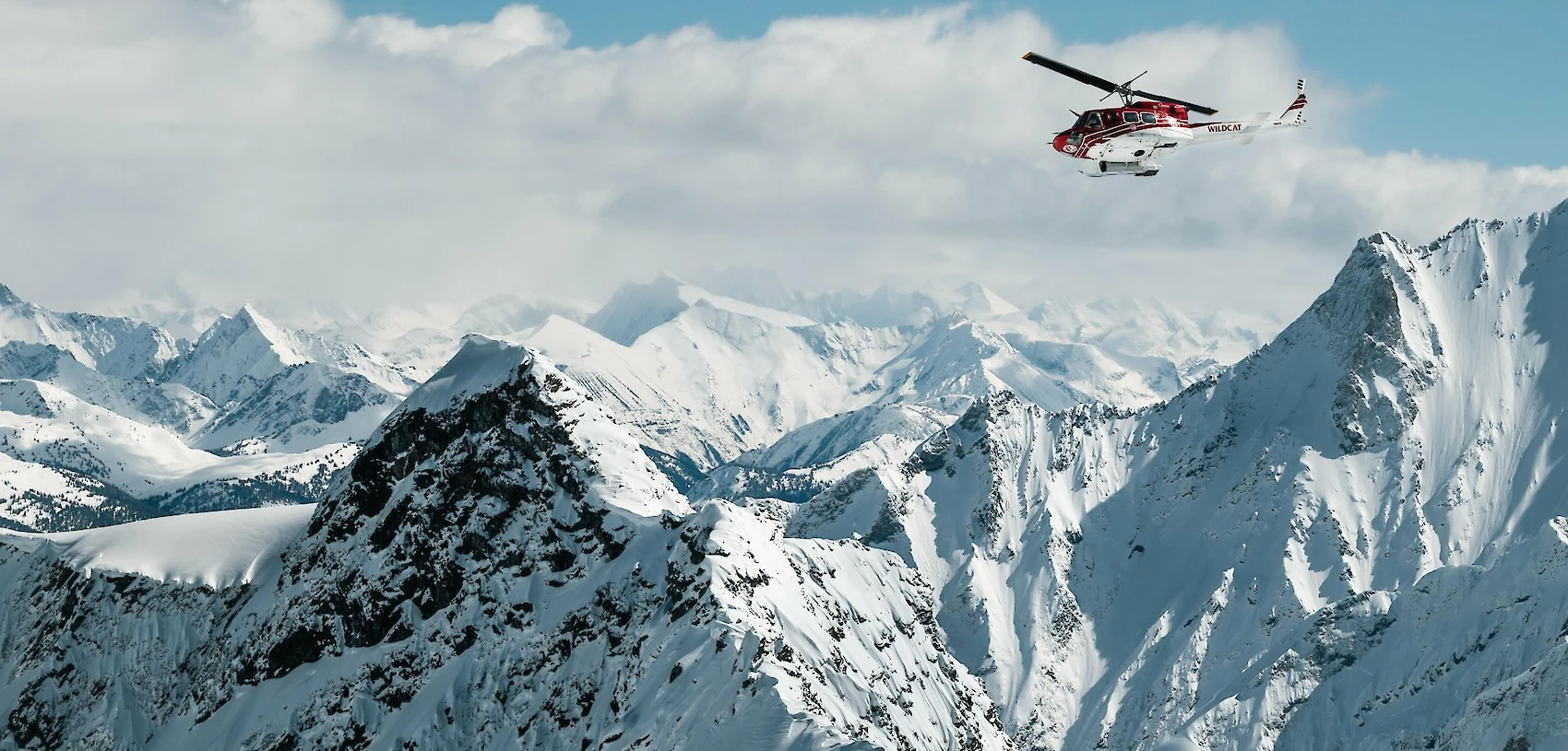 Helicopter soaring above majestic snow-covered mountain peaks under a clear blue sky
