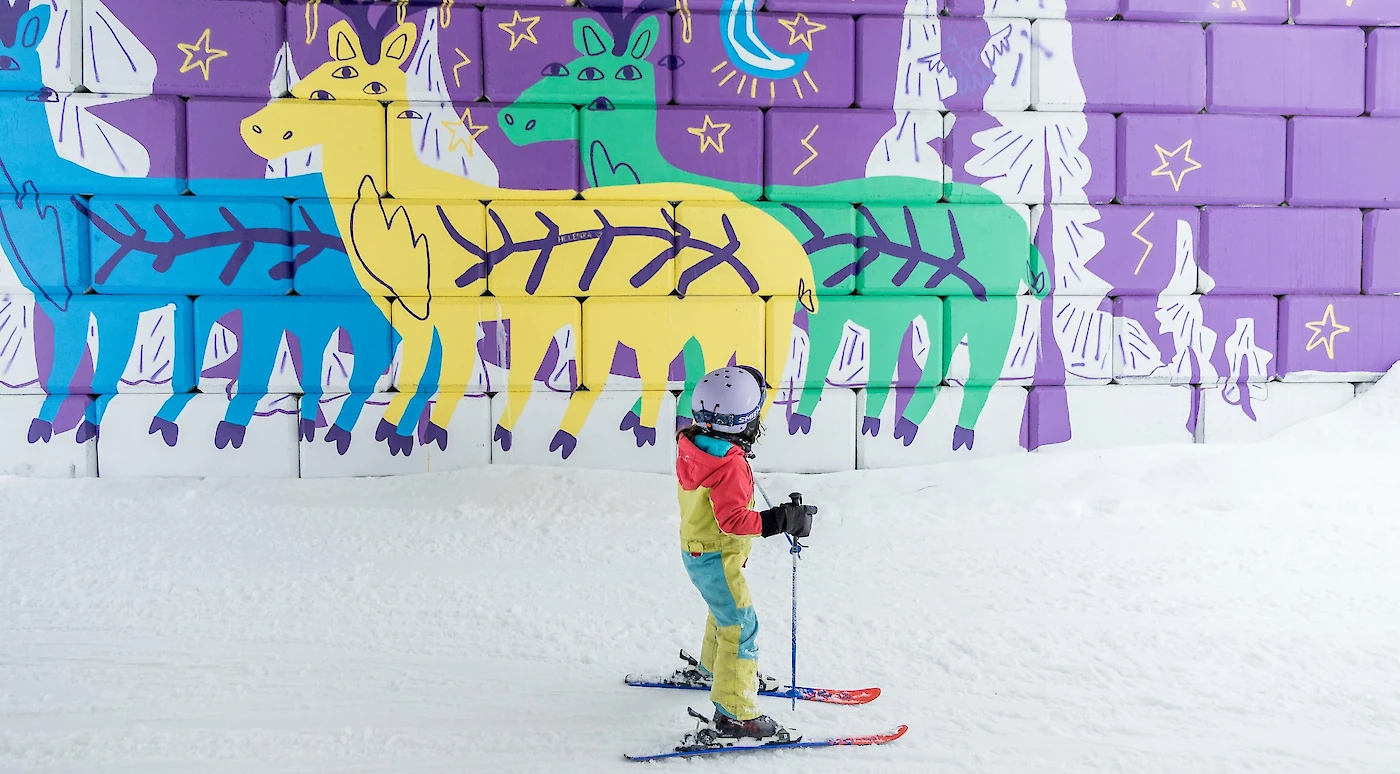 Child skiing with parent on a sunny slope at Revelstoke Mountain Resort during the Kids Ski Free event