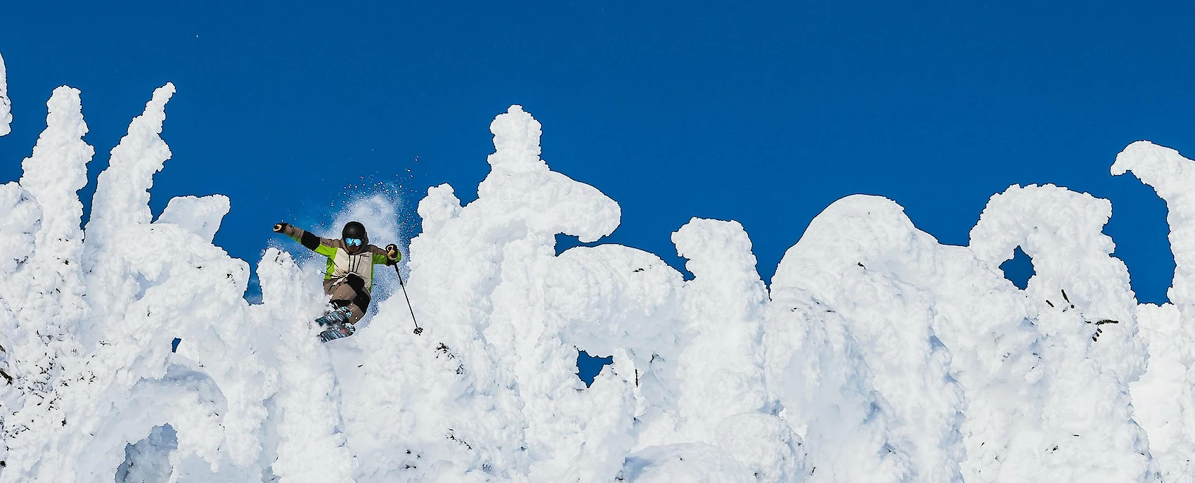 Skier dropping into deep powder through snow-covered glades on a bluebird day at Revelstoke Mountain Resort