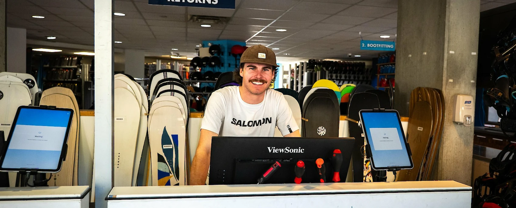 A smiling staff member assisting customers at a snowboard rental station