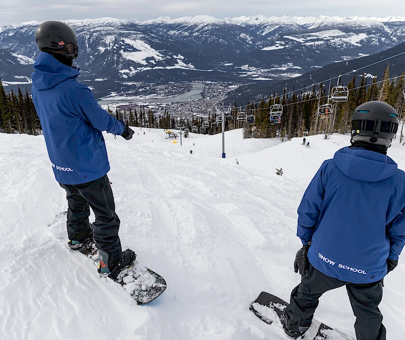 Snowboard instructor and student on a slope with a mountain view